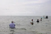 Four men wade-fishing by boat.