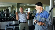 Klaus (Hartmut Volle, l.) stemmt die Hanteln, er m&ouml;chte Reinhard (Bill Mockridge, r.) und Vicky seine Fitness demonstrieren.