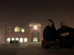 Gwendolin Weisser (links) und Patrick Allgaier sitzen abends am Rand des Platzes vor der erleuchteten Badshahi Moschee in Lahore, Pakistan.