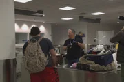 Ein CBP-Beamter kontrolliert das Gep&auml;ck eines Passagiers, w&auml;hrend ein Kameramann am JFK-Flughafen in New York City filmt (National Geographic for Disney)