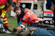 Als Notarzt ist Dr. Ben Ahlbeck (Philipp Danne, r. mit Komparse, l.) heute im Einsatz und trifft auf die verletze Kati Sawal (Souhaila Amade, M.).
