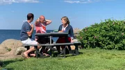 Contributors Will Sweet (L) and Bob Gentile (C) sit with Wendy Fox (R) and learn the best way to crack into a Maine lobster as seen on HGTV's Beachfront Bargain Hunt.