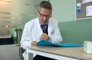 Dr. Kaminski (Udo Schenk) liest die Unterlagen, die angeblich bestätigen, dass Vera Bader eine Tochter hatte. Dr. Kaminski (Udo Schenk) liest die Unterlagen, die angeblich bestätigen, dass Vera Bader eine Tochter hatte.