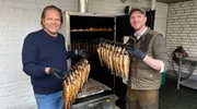 Spitzenkoch Björn Freitag (l.) und Fischwirt Philipp Stobbe (r.) holen den heißgeräucherten Lachs aus dem Räucherofen.