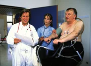 Dr. Stefan Frank (Sigmar Solbach, l.) untersucht zusammen mit Schwester Renate (Ursula Buschhorn) den Bauunternehmer Alfons Meyer (Alexander May).