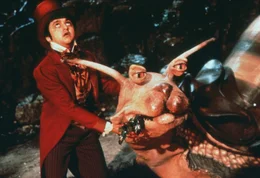 Der lustige Winzling Teeny Weeny (Deep Roy) und seine Rennschnecke sehen erschrocken zu dem riesigen Steinbei&szlig;er auf, der pl&ouml;tzlich vor ihnen steht ...