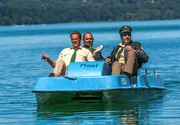 Hubert (Christian Tramitz, l.) und Staller (Helmfried von Lüttichau, r.) sitzen in einem Tretboot und fahren auf den See hinaus. Yazid (Hannes Ringelstetter, M.) sitzt hinter ihnen in Tauchermontur.