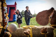Charlie Nelson (Gwilym Lee, r.) und die Gerichtsmedizinerin Kam Karimore (Manjinder Virk, l.) vergnügen sich auf einem Jahrmarkt beim Werfen nach Kokosnüssen.