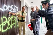 Hubert (Christian Tramitz, links) und Staller (Helmfried von L&uuml;ttichau, rechts) sichern die Beweislage und machen Fotos von den Graffitis. Hubert h&auml;lt einen 10 &euro; Schein als Ma&szlig;stab an die Wand. Hausmeister Heinrich Janker (Hans Stadlbauer) beobachtet das Ganze.