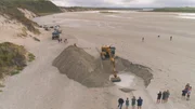 Ein Bagger gräbt ein Loch am Strand Ein Bagger gräbt ein Loch am Strand
