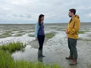 Benedict Feichtner mit Meeresökologin Karin Didderen. Sie will mit moderner Technik die Küstengebiete der Niederlande renaturieren. Die Salzwiesen, die hier neu entstehen, schützen die Dämme vor Erosion und speichern CO2. Benedict Feichtner mit Meeresökologin Karin Didderen. Sie will mit moderner Technik die Küstengebiete der Niederlande renaturieren. Die Salzwiesen, die hier neu entstehen, schützen die Dämme vor Erosion und speichern CO2.