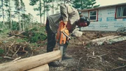 Matty schneidet Holzst&auml;mme mit einer Kettens&auml;ge, bereitet sie vor und formt sie nach dem Plan f&uuml;r eine neue Blockh&uuml;tte
