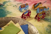 Namenskärtchen-Elefanten im Hindi-Stil auf mit Holi-Farben koloriertem Tischtuch.