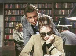 Der verkrachte Schriftsteller Paul Varjak (George Peppard) besucht Holly Golightly (Audrey Hepburn) in der Stadtbibliothek, wo sie sich &uuml;ber das Land ihres k&uuml;nftigen Million&auml;rsgatten informiert.
