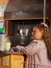 Recre of Kristine staging and filming Natalia as she sits at kitchen with coffe and cleaner on counter.