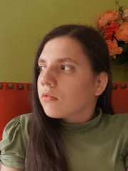 Medium shot of Natalia wearing a green shirt from intv. Sitting in red chair, looking to her right.