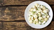 Potato salad with eggs and green onion on white plate over wooden background with copy space. Top view, flat lay food