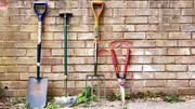 A Spade, edging tool, fork and some shears leaning against a garden wall made of bricks.