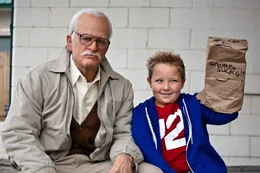 Nach den neckischen Streitereien sitzen Zisman (Johnny Knoxville, l.) und Billy (Jackson Nicoll, r.) nebeneinander wobei Billy eine T&uuml;te mit der Aufschrift "Grampa sucks!!!" in der Hand h&auml;lt.