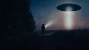 Ein Science-Fiction-Konzept eines Mannes mit einer Taschenlampe, der ein au&szlig;erirdisches UFO betrachtet. Schwebend &uuml;ber einem Feld in einer gespenstischen, nebligen Nacht auf dem Lande.