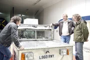 V.l.: Richard Hammond, Jeremy Clarkson und James May stehen an dem Elektroauto in einem Tunnel.