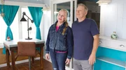 Bargain hunters Betteanne (L) and Ed (R) soak in the vacay vibes of Bay Breeze's bright blue living room, as seen on HGTV's original series, Beachfront Bargain Hunt.