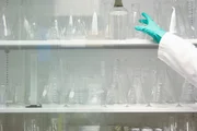 Scientist reaching for flask on laboratory shelf