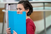 Rebecca (Milena Straube) versucht heimlich etwas zu beobachten und h&auml;lt sich dazu eine Aktenmappe vors Gesicht.