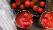 Fresh cherry tomatoes (on the vine) and two open cans of tomatoes on a kitchen counter