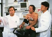 Dr. Stefan Frank (Sigmar Solbach, l.) und der Kardiologe Dr. Thomas Reinhardt (Christopher Barker, r.) untersuchen Chefarzt Dr. Ulrich Waldner (Hartmut Becker) nach dem Einsetzen des Herzschrittmachers.