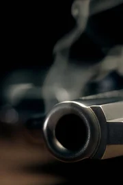 A gritty crime scene image of a smoking hand gun, revolver, lying on the floor with narrow focus on the tip if the barrel and dark background