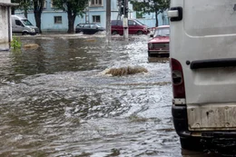 riving car on flooded road during flood caused by torrential rains. Cars float on water, flooding streets. Splash on car. Flooded city road with large puddle.  Flooding after heavy rains at city
