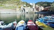 Bunte Fischerboote schaukeln im Hafen von Vernazza &ndash; eingerahmt von pastellfarbenen H&auml;usern, steilen Weinterrassen und der markanten Kirche Santa Margherita d&rsquo;Antiochia.