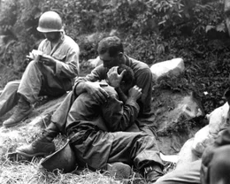 Ein trauernder amerikanischer Infanterist, dessen Kumpel im Kampf gefallen ist, wird von einem anderen Soldaten getr&ouml;stet. Im Hintergrund f&uuml;llt ein Sanit&auml;ter methodisch die Verletztenschilder aus, Gebiet Haktong-ni, Korea. 28. August 1950.