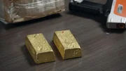 Goldbarren werden auf einen Inspektionstisch gelegt, w&auml;hrend HSI-Agenten in der N&auml;he eine Nachbesprechung &uuml;ber einen untersuchten illegalen Goldabbau in Miami durchf&uuml;hren.
