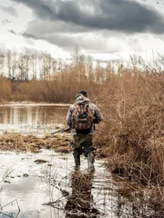 Hunter man in camouflage with shotgun exploring wetland area for prey during hunting period
