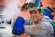 Portrait of Mike Rowe next to venting gas on torch bottles. Notice sticker "Pressure Building".