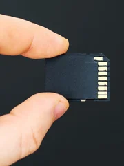 Male hand holding SD card on black background.