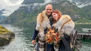 The newlyweds Caroline & Simon are posing in front of the water in their traditional viking wedding gowns. They are cuddled up and looking half smiling into the camera while Caroline is holding her bridal flower bouquet. The newlyweds Caroline & Simon are posing in front of the water in their traditional viking wedding gowns. They are cuddled up and looking half smiling into the camera while Caroline is holding her bridal flower bouquet.
