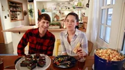 Candid shot of Molly Yeh and her husband Nick at dinner table with Sausage, Peppers, Onion Deep Dish Pizza, Mint Truffle Bars, Caramel Cheddar Popcorn, & Chicago Corn Dogs, as seen on Girl Meets Farm, Season 7.
