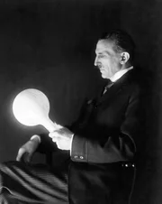 Nikola Tesla (18561943) mit einer von ihm in den 1890er-Jahren entwickelten gasgef&uuml;llten, phosphorbeschichteten kabellosen Lampe. Aufnahme von 1919.