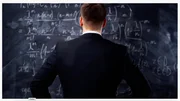 Ein Mann steht vor einer Tafel, die mit komplexen mathematischen Formeln und Gleichungen bedeckt ist.