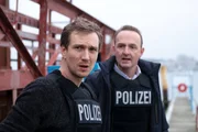 Simon Brandt (Jan Krauter, l.) und Jan Geissler (Peter Jordan, r.) sind zu einem Polizeieinsatz am Hafen gekommen. Die beiden beobachten die Bootsanleger.