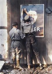 Von Tausenden Plakaten und Litfa&szlig;s&auml;ulen starrt Hitlers Konterfei mit B&auml;rtchen und Seitenscheitel auf die W&auml;hlerinnen und W&auml;hler.