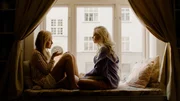 Natalie (Mina Dale, l.) und Selina (Elli Rhiannon M&uuml;ller Osborne, r.) sitzen sich gem&uuml;tlich auf einer Fensterbank gegen&uuml;ber. Sie sind in ein Gespr&auml;ch vertieft und schmieden einen Plan, um ihr makelloses Image zu retten.