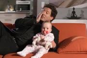 Christoph Baumgartner (Francis Fulton-Smith) sieht mit dem Baby Rosi eine Sendung im TV, in der seine Freundin Chantal interviewt wird.