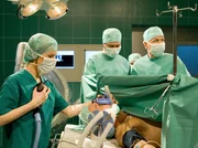 Als Dr. Roland Heilmann (Thomas R&uuml;hmann, rechts); Dr. Kathrin Globisch ( Andrea Kathrin Loewig, links) und Dr. Philipp Brentano (Thomas Koch, Mitte) Hartmut Gro&szlig; (Uwe Karpa, liegend) operieren, stellt Roland eine schwere Nervensch&auml;digung fest. Es ist fraglich, ob Hartmut Gro&szlig; den Arm jemals wieder voll benutzen kann.