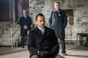 Nachdem ein kleines M&auml;dchen aus ihrem Haus entf&uuml;hrt und ihr Vater ermordet wurde, hoffen Holmes (Jonny Lee Miller, M.) und Capt. Gregson (Aidan Quinn, r.), im Gef&auml;ngnis etwas von Moriarty dar&uuml;ber zu erfahren. Moriartys Aufpasser Agent Mattoo (Faran Tahir, l.) beh&auml;lt die Gefangene dabei stets im Auge ...