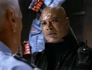 Von SG-3 kehren nur drei Mitglieder zurück, darunter auch Teal'c (Christopher Judge, re). Sie haben unter großen Verlusten Naquada für General Bauer (Lauwrence Dane) und seine Experimente besorgt... Als General Hammond dem entsetzten Team seinen Rücktritt bekannt gibt, ahnt O'Neill, dass mehr dahinter stecken muss, als die Sehnsucht des Generals nach Ruhe. Tatsächlich ergeben seine Nachforschungen, dass Hammond von oberster Stelle abkommandiert wurde, weil er sich weigerte, extraterrestrische Technologie um jeden Preis für die Menschheit verfügbar zu machen. Hammond wird durch den skrupellosen General Bauer ersetzt, der als erstes das SG-1-Team auflöst und Carter damit beauftragt eine Bombe zu bauen, die in der Lage ist, ganze Planeten zu zerstören. O'Neill erkennt, dass es wirklich an der Zeit ist, die Dinge wieder gerade zu rücken. Doch um das NID schachmatt zu setzen und Hammond zurückzuholen, muss er ausgerechnet mit Colonel Maybourne zusammen arbeiten. Von SG-3 kehren nur drei Mitglieder zurück, darunter auch Teal'c (Christopher Judge, re). Sie haben unter großen Verlusten Naquada für General Bauer (Lauwrence Dane) und seine Experimente besorgt... Als General Hammond dem entsetzten Team seinen Rücktritt bekannt gibt, ahnt O'Neill, dass mehr dahinter stecken muss, als die Sehnsucht des Generals nach Ruhe. Tatsächlich ergeben seine Nachforschungen, dass Hammond von oberster Stelle abkommandiert wurde, weil er sich weigerte, extraterrestrische Technologie um jeden Preis für die Menschheit verfügbar zu machen. Hammond wird durch den skrupellosen General Bauer ersetzt, der als erstes das SG-1-Team auflöst und Carter damit beauftragt eine Bombe zu bauen, die in der Lage ist, ganze Planeten zu zerstören. O'Neill erkennt, dass es wirklich an der Zeit ist, die Dinge wieder gerade zu rücken. Doch um das NID schachmatt zu setzen und Hammond zurückzuholen, muss er ausgerechnet mit Colonel Maybourne zusammen arbeiten.
