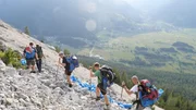 Eine Gruppe von Wanderern steigt mit Trekkingst&ouml;cken einen steinigen Hang hinauf.
